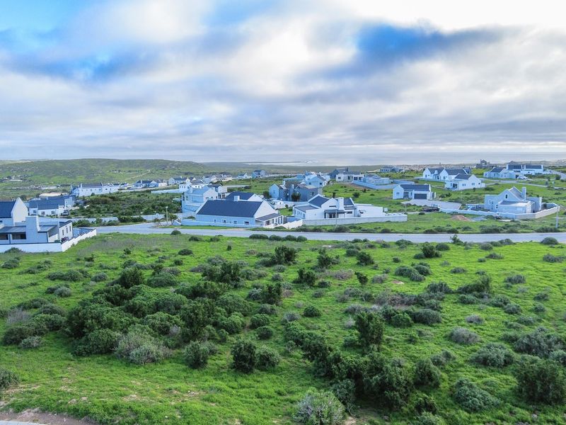 An aerial view of a coastal residential estate featuring modern houses with dark roofs set within a natural, green landscape.