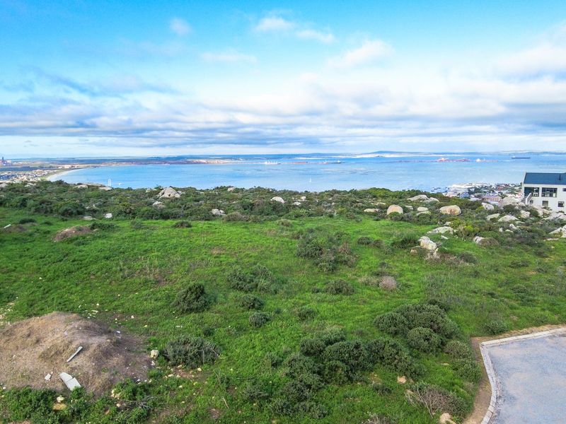 Elevated aerial view showcasing the coastal landscape, natural vegetation, and surrounding residential area with a clear outlook over the bay.