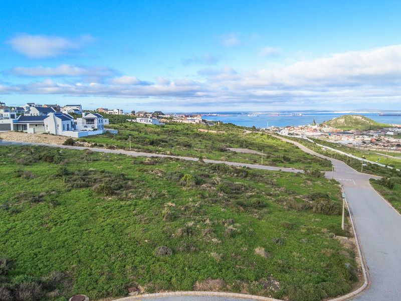 An elevated aerial view of the coastal estate, showcasing the surrounding landscape, nearby residential properties, and distant ocean views.