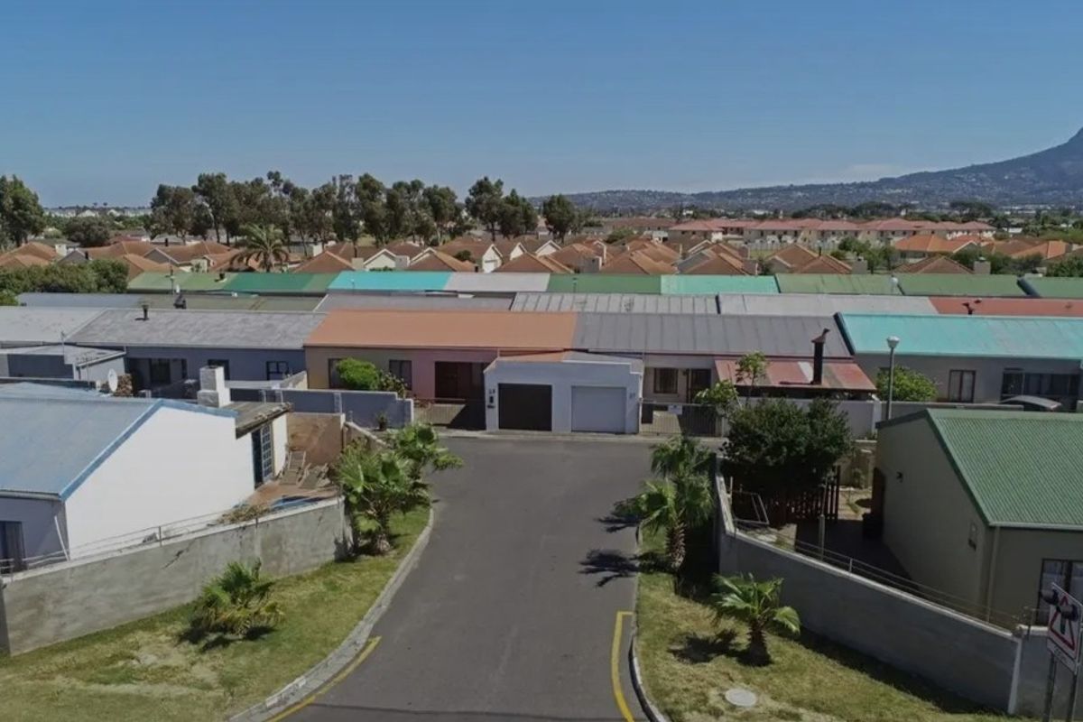 Aerial view of a residential street featuring a row of houses with varied roof colors and a paved access road.