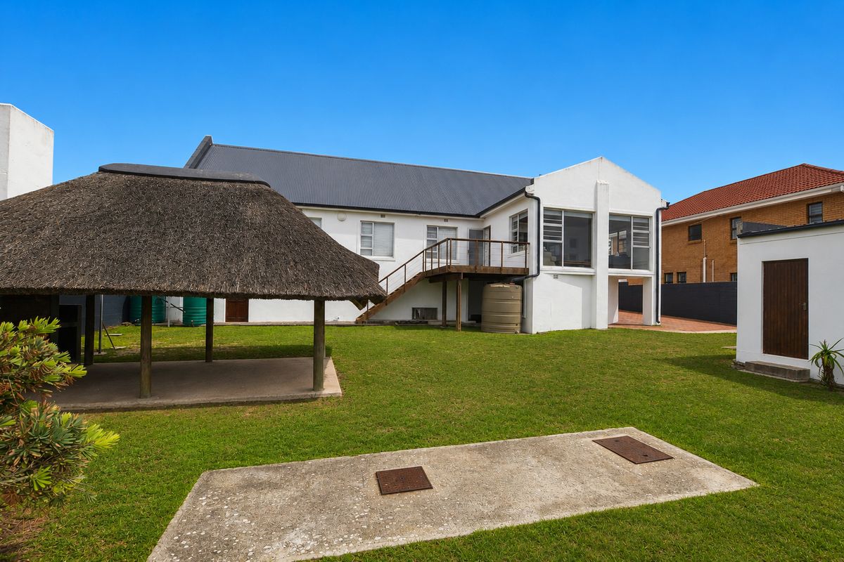 Rear view of the property featuring a thatched lapa, elevated wooden deck, and a spacious lawn area.