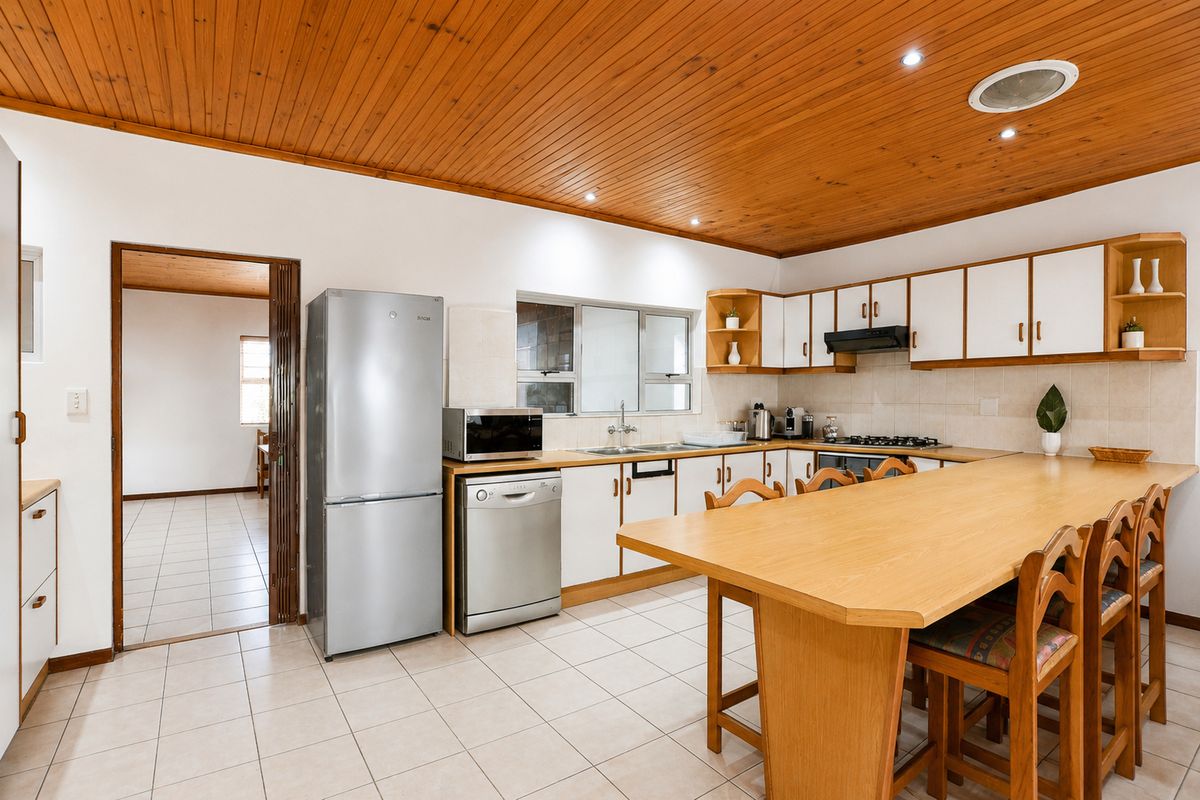 A functional kitchen featuring white cabinetry, a timber breakfast bar, tiled flooring, and a distinctive timber-paneled ceiling with recessed lighting.