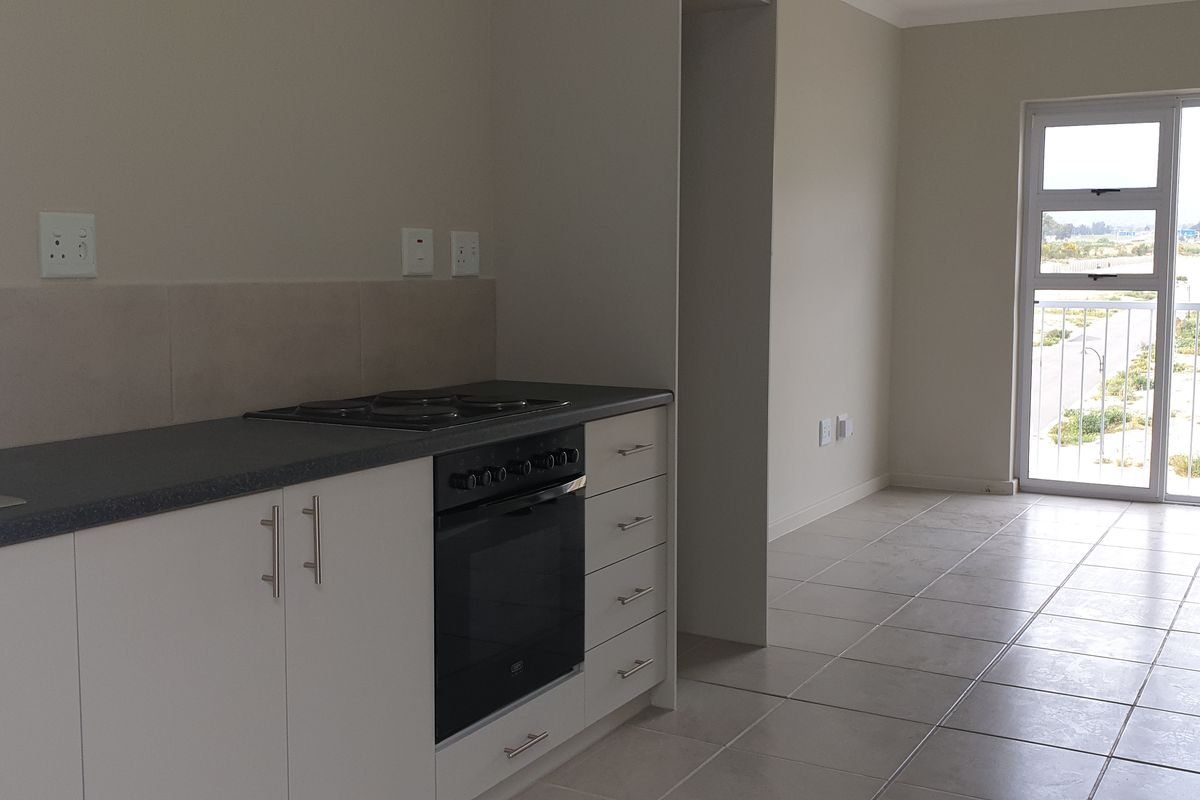 An open-plan kitchen and living area featuring tiled floors, modern white cabinetry, built-in oven and hob, and a sliding door leading to a balcony.