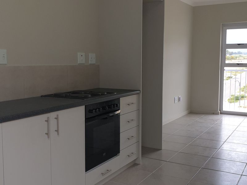 An open-plan kitchen and living area featuring tiled floors, modern white cabinetry, built-in oven and hob, and a sliding door leading to a balcony.
