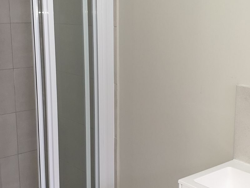 A modern, clean bathroom featuring a glass-enclosed shower, neutral wall and floor tiling, and a white vanity cabinet with an integrated basin.