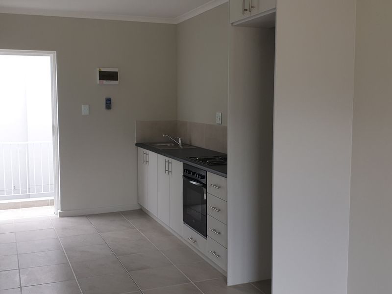 An open-plan kitchen area featuring modern built-in cabinetry, a built-in oven, hob, and tiled flooring, with direct access to an outdoor balcony.