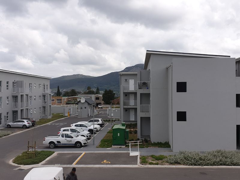 An elevated view of a modern apartment complex featuring paved parking areas, external staircases, and landscaped grounds with mountain views in the background.