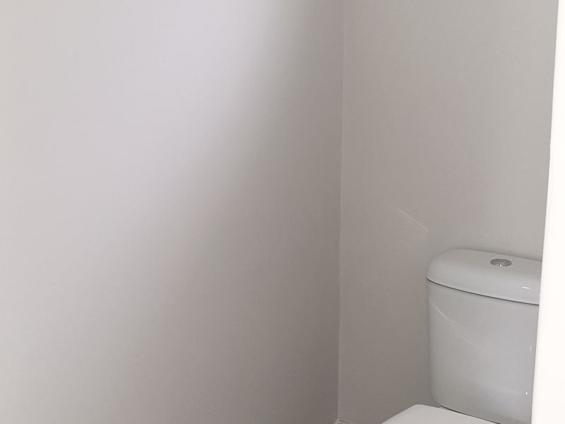 A clean and minimalist powder room featuring neutral wall tones, tiled flooring, and a modern white toilet suite.
