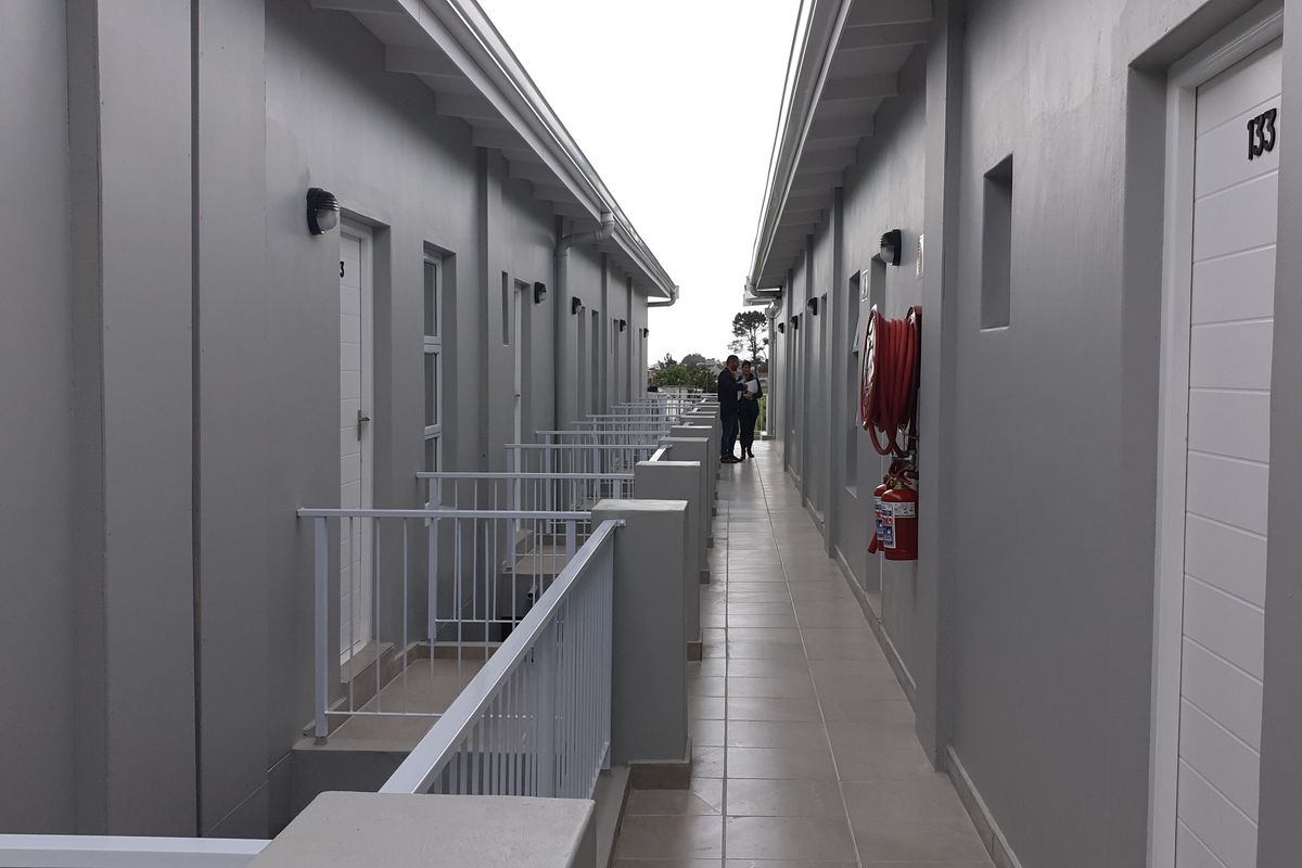 An exterior apartment hallway featuring tiled flooring, metal safety railings, and wall-mounted fire safety equipment.