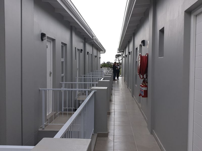 An exterior apartment hallway featuring tiled flooring, metal safety railings, and wall-mounted fire safety equipment.