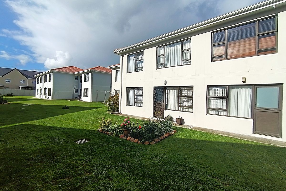 A view of the rear elevation of a multi-story apartment building featuring well-maintained lawns and established garden beds.