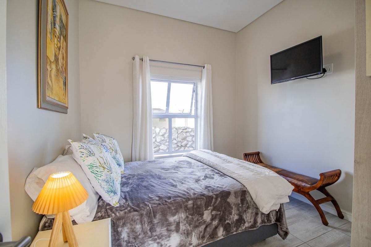 A well-maintained bedroom featuring tiled flooring, a window with curtains, and a wall-mounted television.