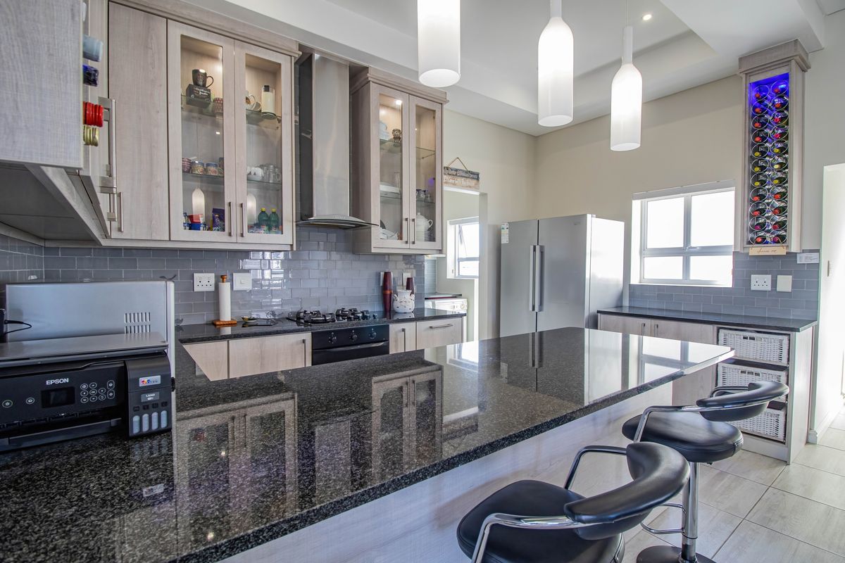 Modern kitchen featuring granite countertops, subway tile backsplash, built-in cabinetry, gas hob, and integrated wine rack with stylish pendant lighting.