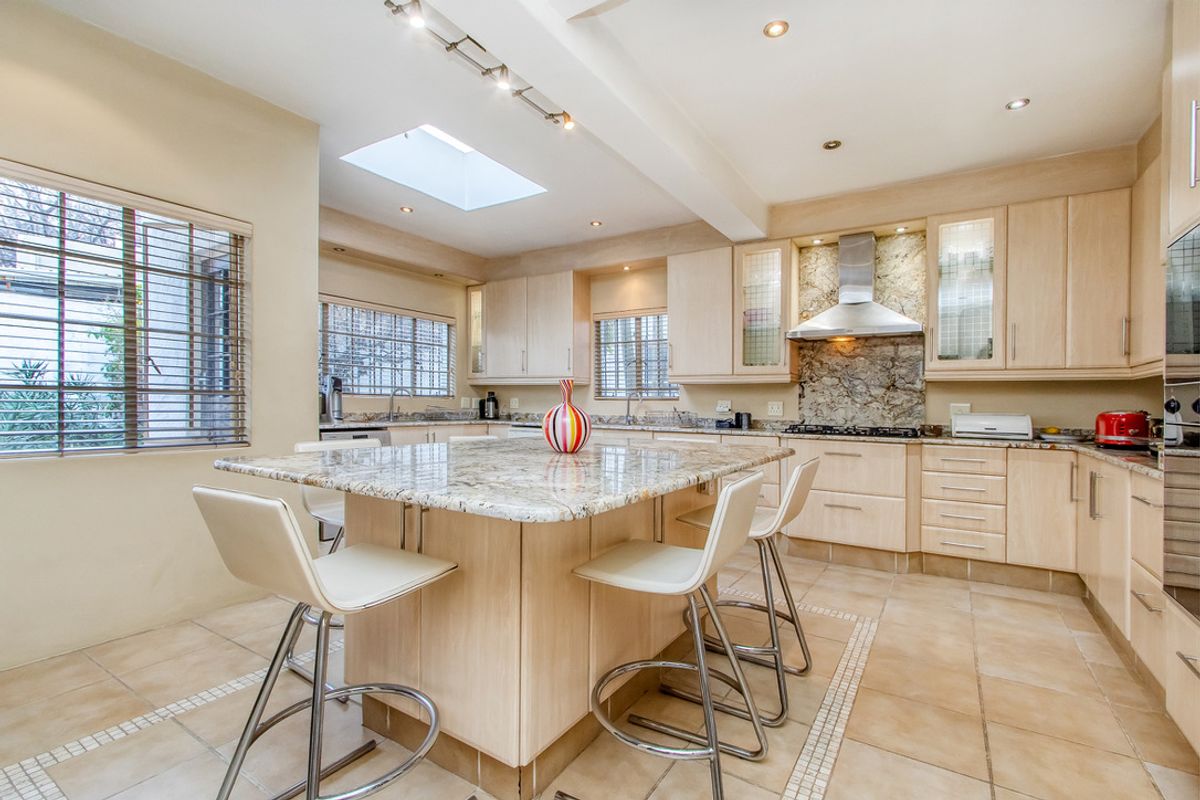 Spacious kitchen featuring light wood cabinetry, granite countertops, a central island with breakfast bar seating, and a built-in stainless steel extractor fan.