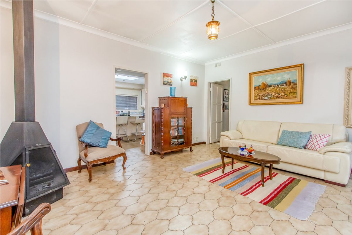 A living room featuring a freestanding fireplace, tiled flooring, and access to an adjacent kitchen area.