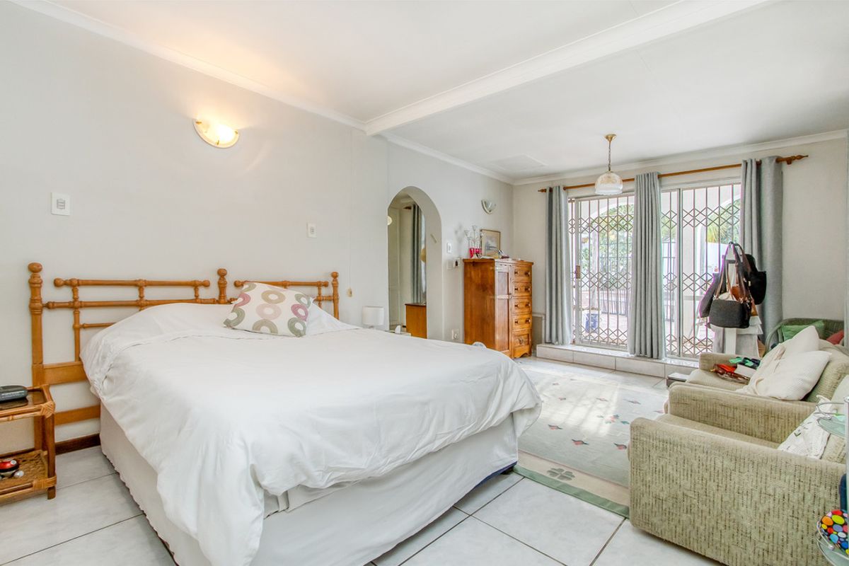 Spacious bedroom featuring tiled flooring, arched doorway access, and sliding glass doors with security gates leading to an outdoor area.