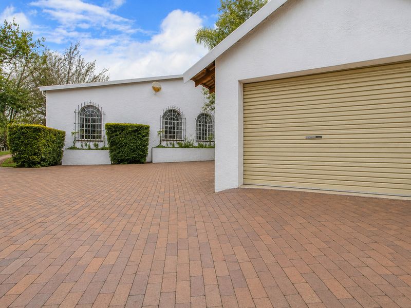 Exterior view of the property featuring a paved driveway, a single garage with a roller door, and white rendered walls with arched windows.