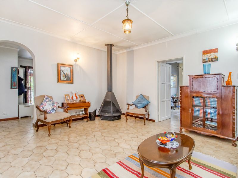 A living room featuring a freestanding metal fireplace, tiled flooring, and arched doorway access to adjacent living spaces.