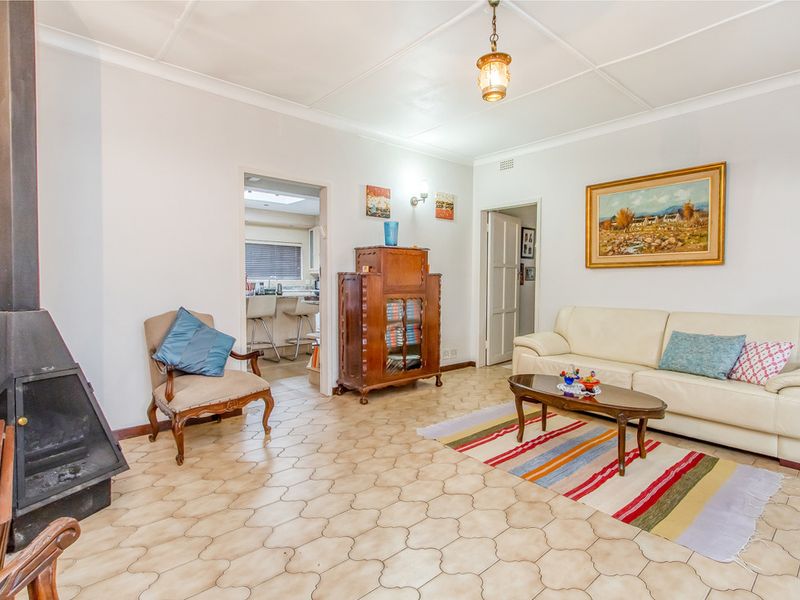 A living room featuring a freestanding fireplace, tiled flooring, and access to an adjacent kitchen area.