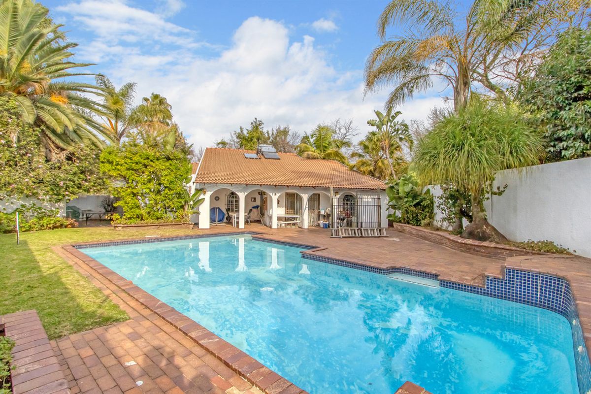 Rear view of the property featuring a swimming pool, brick-paved patio area, and a covered veranda with arched architectural details.
