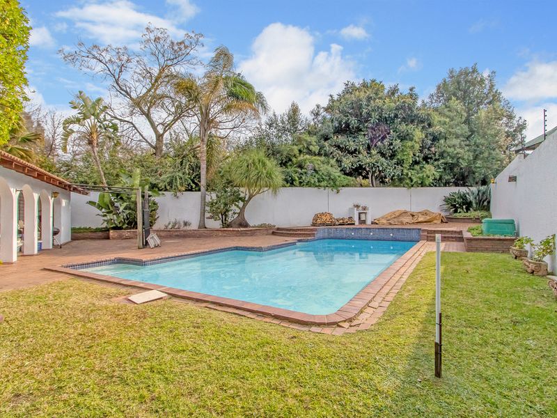 Outdoor pool area featuring a rectangular swimming pool, paved surround, and a covered patio area set within a private garden.