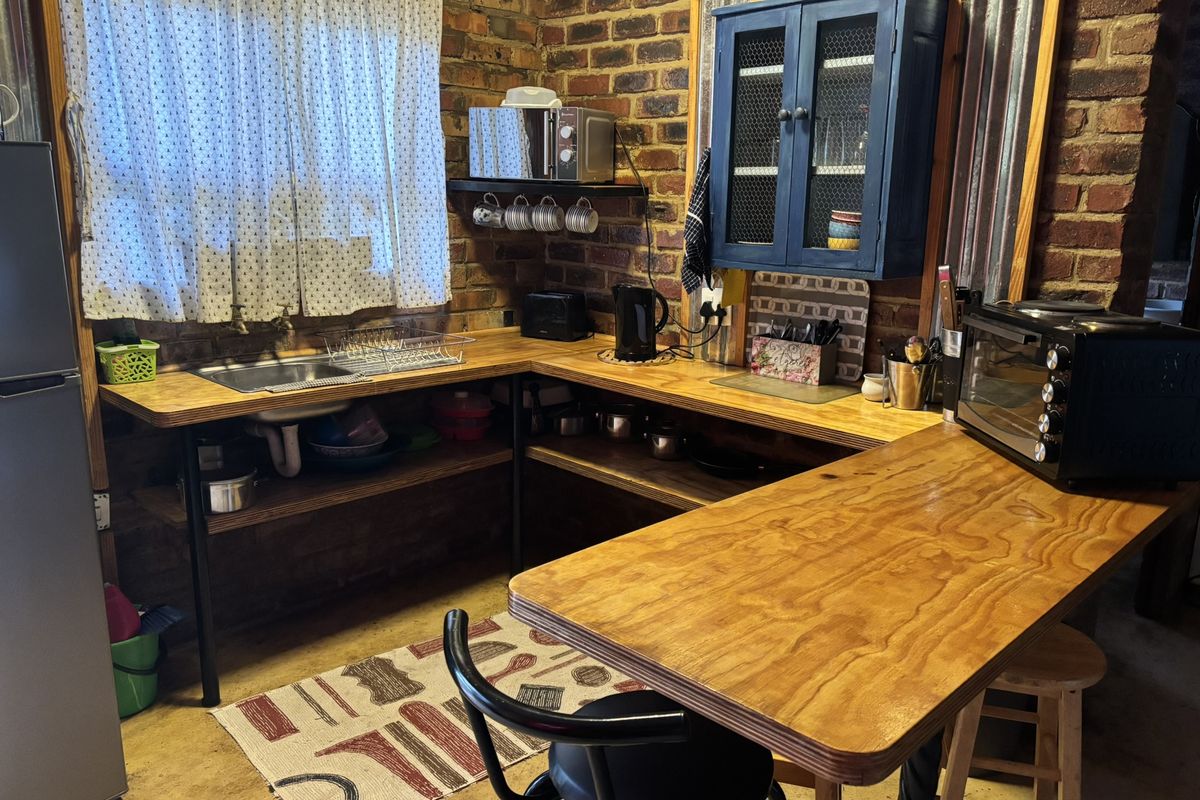 Rustic kitchen area featuring exposed brick walls, timber countertops, open shelving, and a built-in wall cabinet.