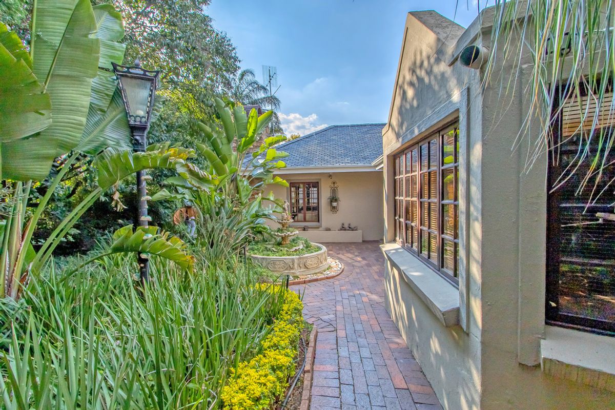 A charming rear garden area featuring brick pathways, a central stone fountain, and lush landscaping alongside the main building structure.