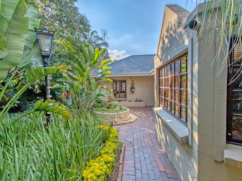 A charming rear garden area featuring brick pathways, a central stone fountain, and lush landscaping alongside the main building structure.