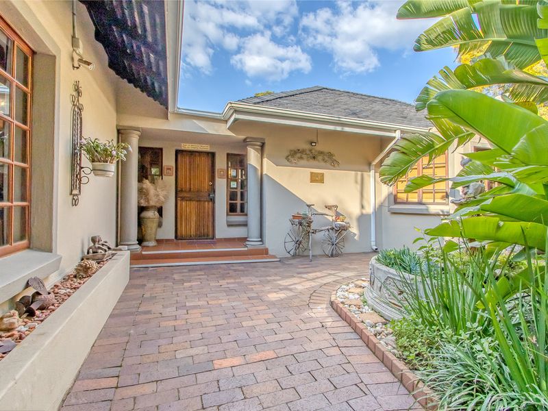 A welcoming front entrance featuring a brick-paved walkway, decorative columns, and a solid wooden door, set within a well-maintained garden area.