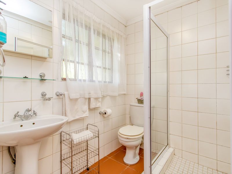 A functional bathroom featuring a pedestal basin, a shower enclosure, and tiled finishes throughout, offering a clean and practical layout.