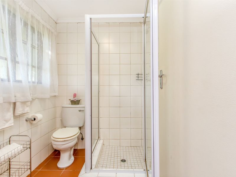 A functional bathroom featuring a shower enclosure, toilet, and tiled finishes, offering a clean but dated aesthetic suitable for modernization.