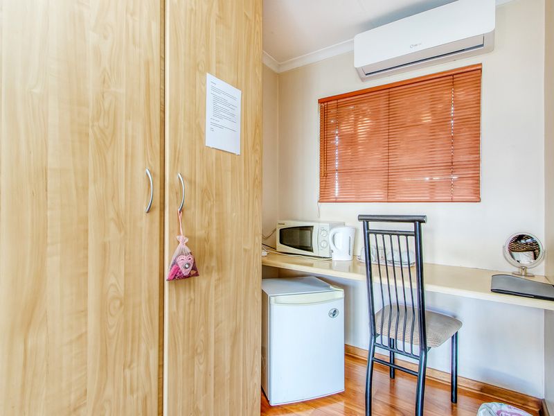 A compact bedroom area featuring a built-in wardrobe, a functional desk space, and a wall-mounted split-system air conditioner for climate control.