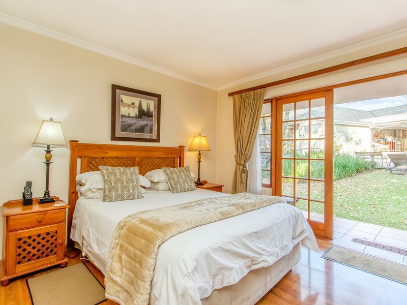 A well-maintained bedroom featuring wooden flooring and direct access to a private patio through wooden-framed french doors.