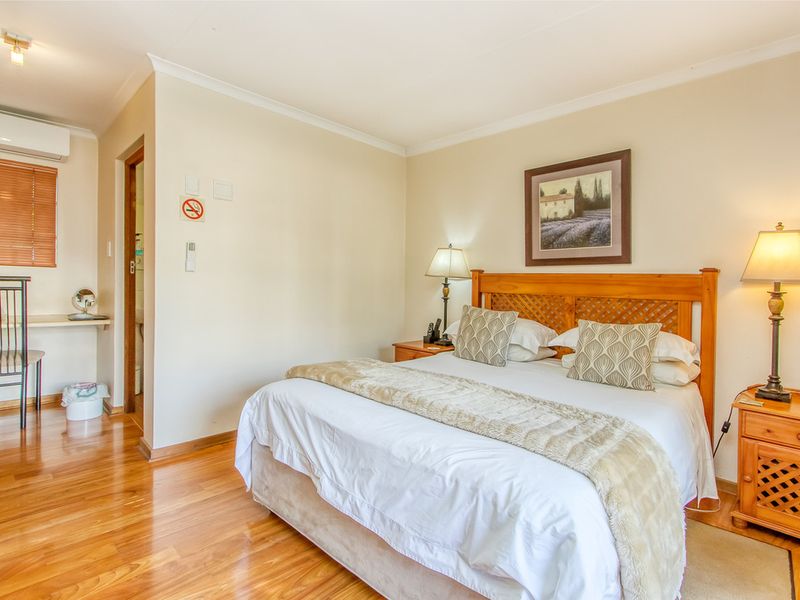 A well-maintained bedroom featuring warm laminate flooring, a built-in desk area, and a split-system air conditioning unit for climate control.