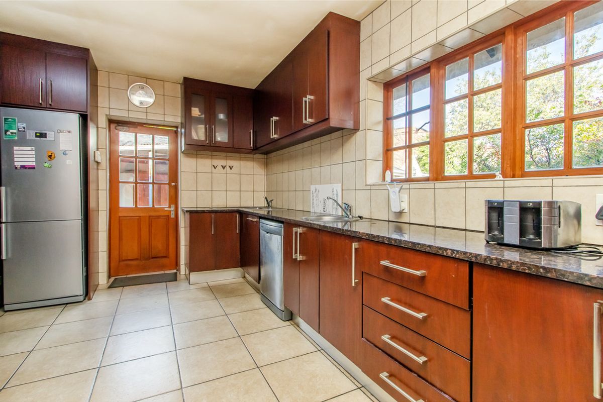 A functional kitchen featuring dark wood cabinetry, granite countertops, tiled flooring, and direct access to the exterior via a timber-framed door.