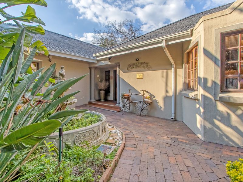 A charming front entrance area featuring a brick-paved walkway, a decorative stone fountain, and well-maintained exterior walls with classic wooden window frames.