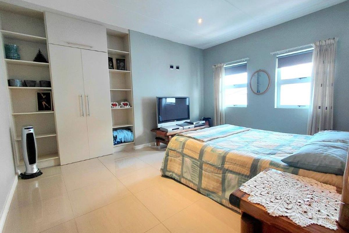 A well-lit bedroom featuring built-in floor-to-ceiling cabinetry with integrated shelving, tiled flooring, and dual windows allowing for natural light.