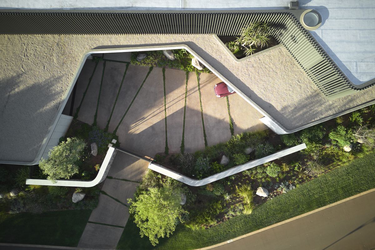 An aerial view of the property entrance, showcasing modern architectural design, landscaped gardens, and a paved driveway.
