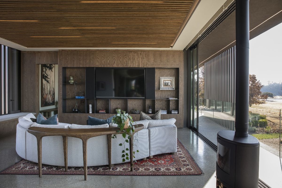 Modern living room featuring a timber-slatted ceiling, built-in cabinetry, polished concrete flooring, and a freestanding fireplace, with large sliding glass doors opening to the exterior.