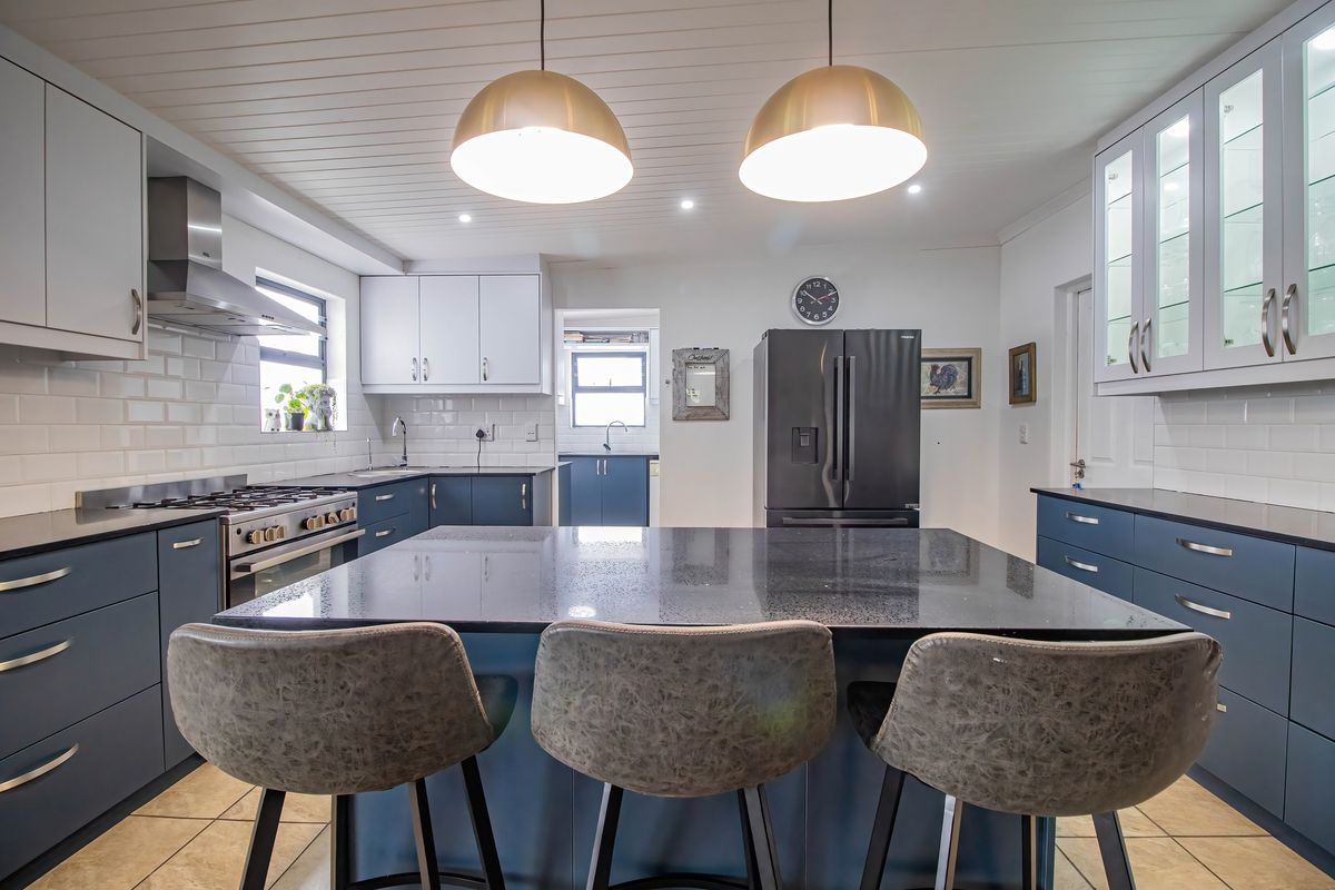 Modern kitchen featuring a large central island with stone countertop, dark blue cabinetry, subway tile backsplash, and stainless steel gas range with extractor fan.