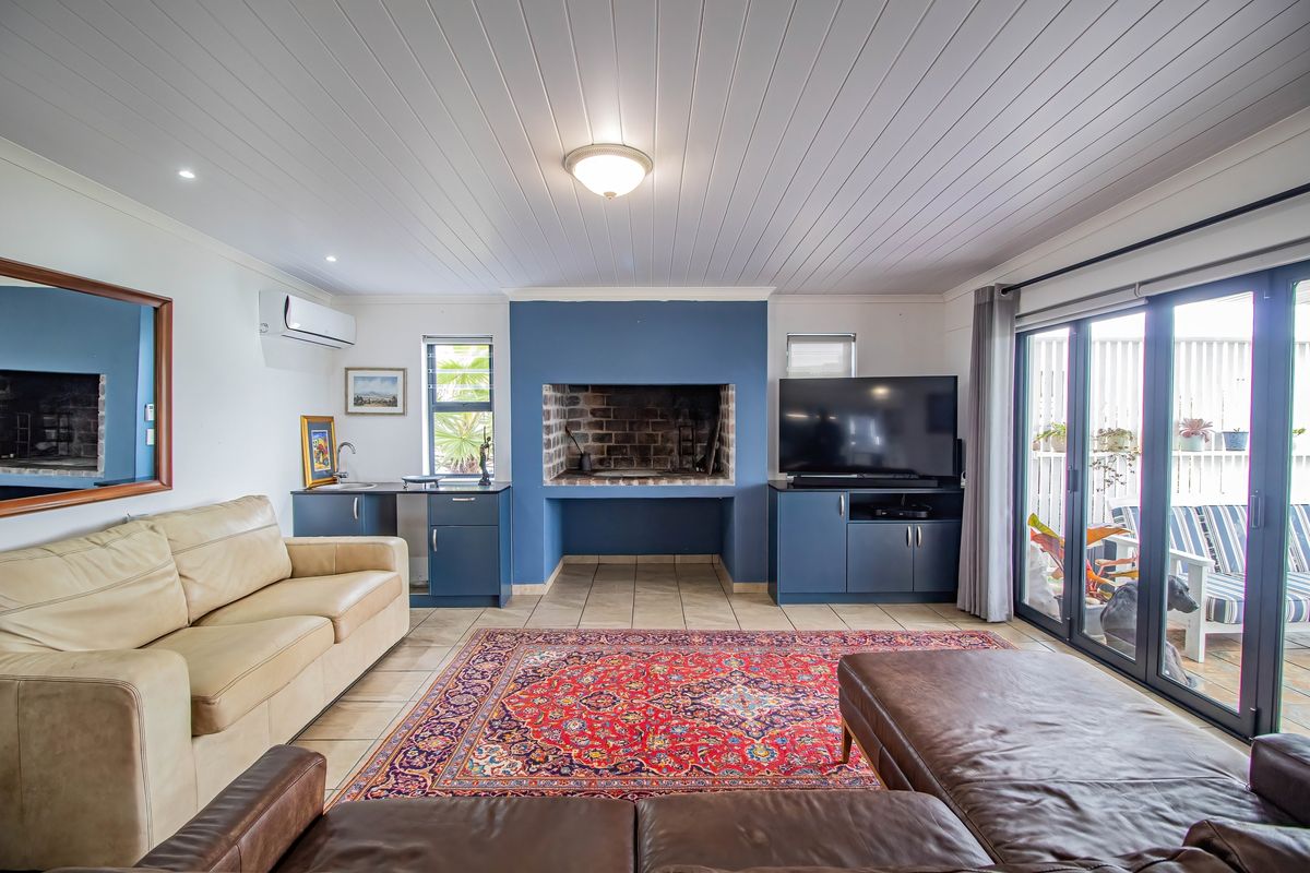 Spacious living room featuring a built-in indoor braai, tiled flooring, and large glass sliding doors providing seamless access to the outdoor patio area.