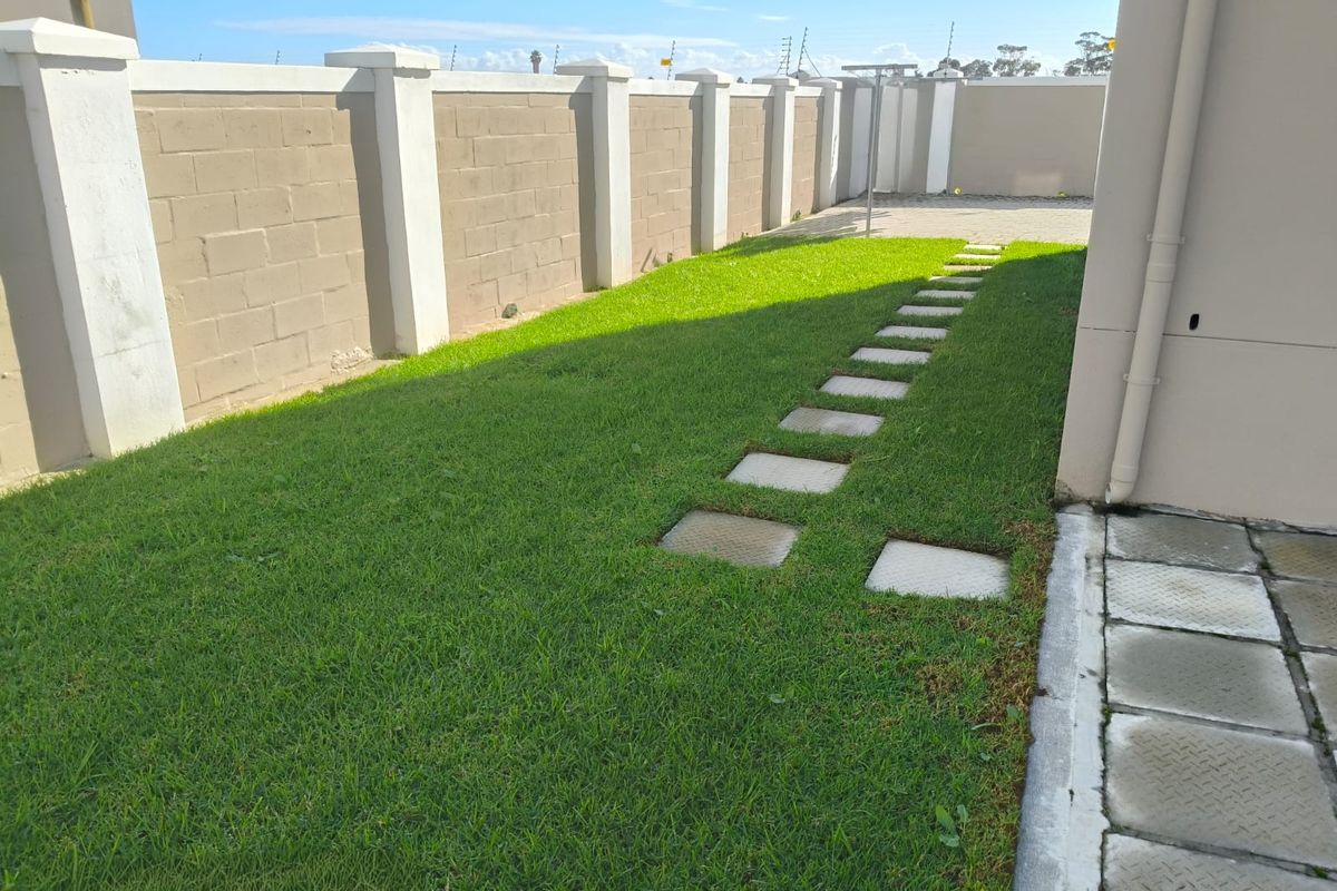 A well-maintained rear garden featuring a manicured lawn, concrete stepping stones, and a secure perimeter boundary wall.