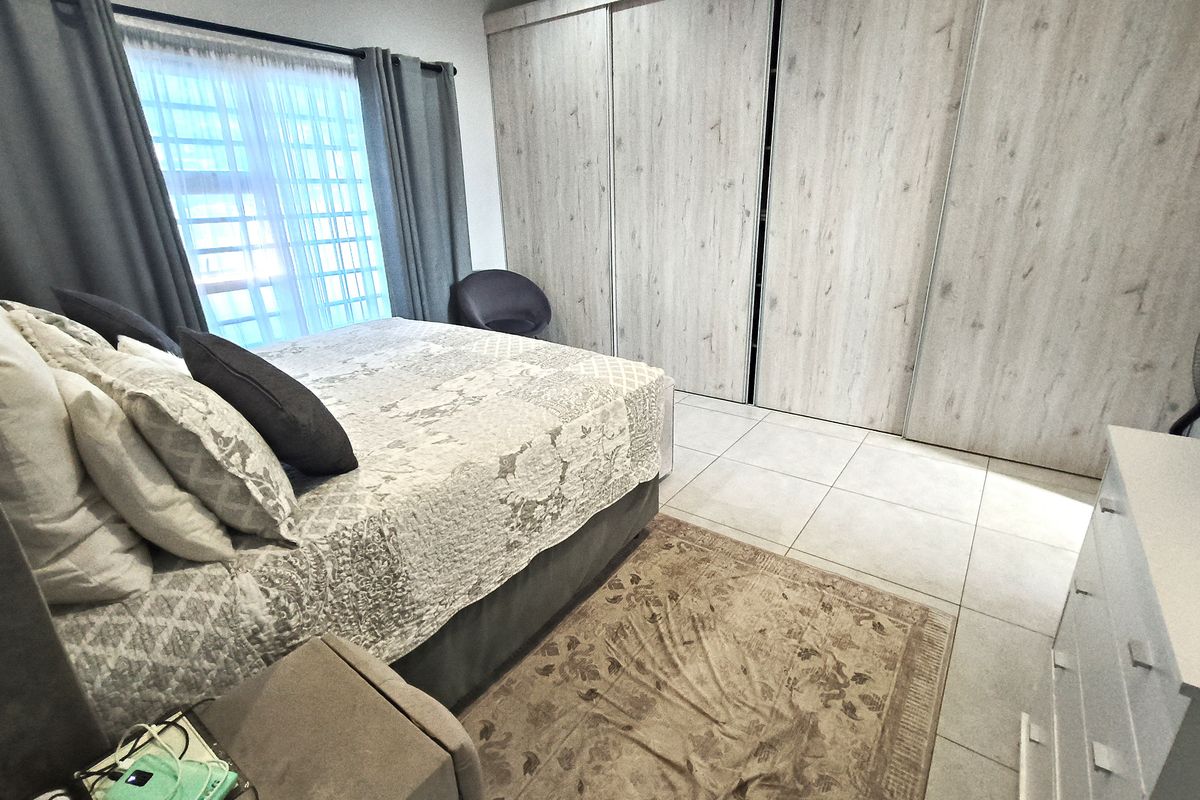 A well-maintained bedroom featuring large built-in wooden wardrobes, tiled flooring, and a window with curtain treatments.