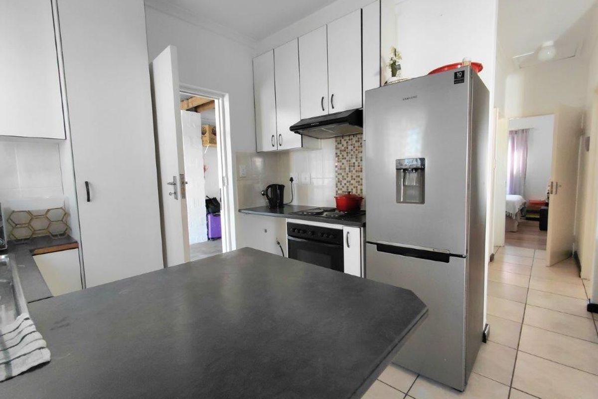 A functional kitchen featuring white cabinetry, dark countertops, a built-in oven with extractor fan, and tiled flooring, leading to an adjacent room.