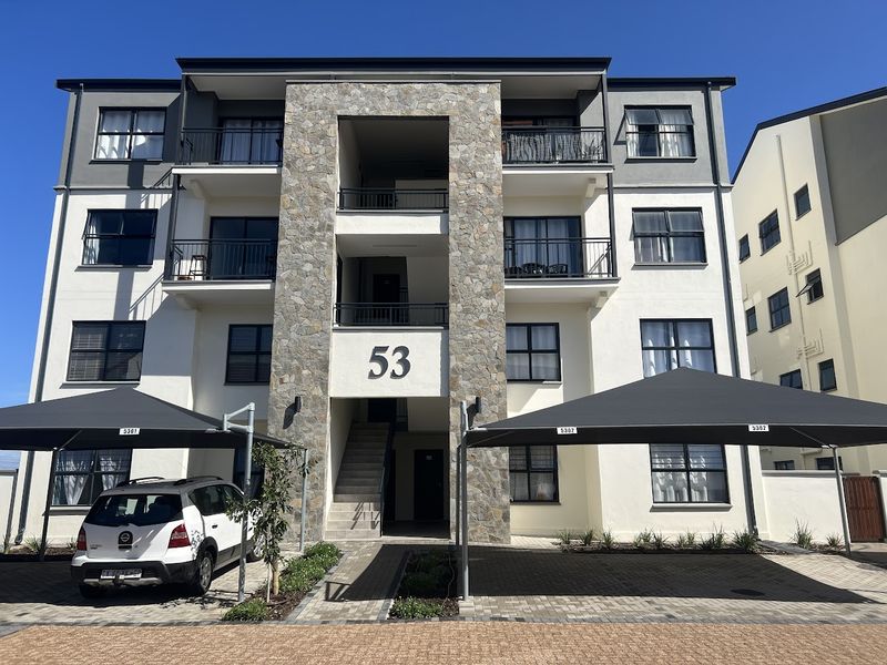 Front elevation of a modern apartment building featuring stone cladding, private balconies, and dedicated covered parking bays.