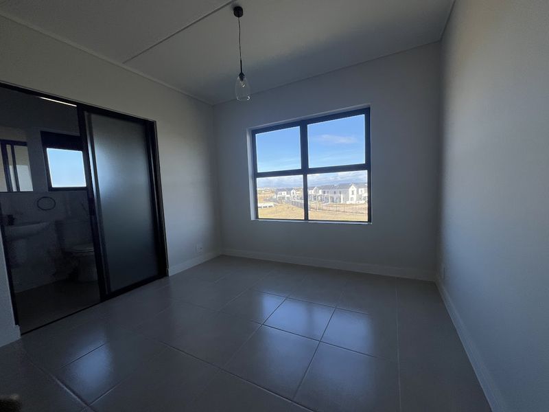 A bright, empty bedroom featuring tiled flooring, a modern pendant light, and a sliding glass door leading to an en-suite bathroom.