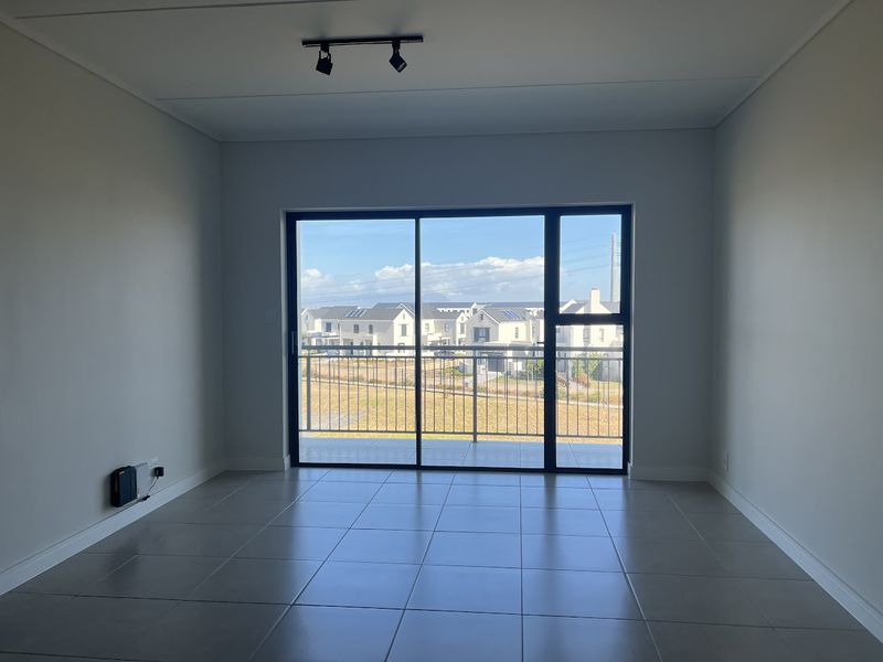 A bright, empty living area featuring large sliding glass doors that open onto a balcony with neighborhood views and modern tiled flooring.