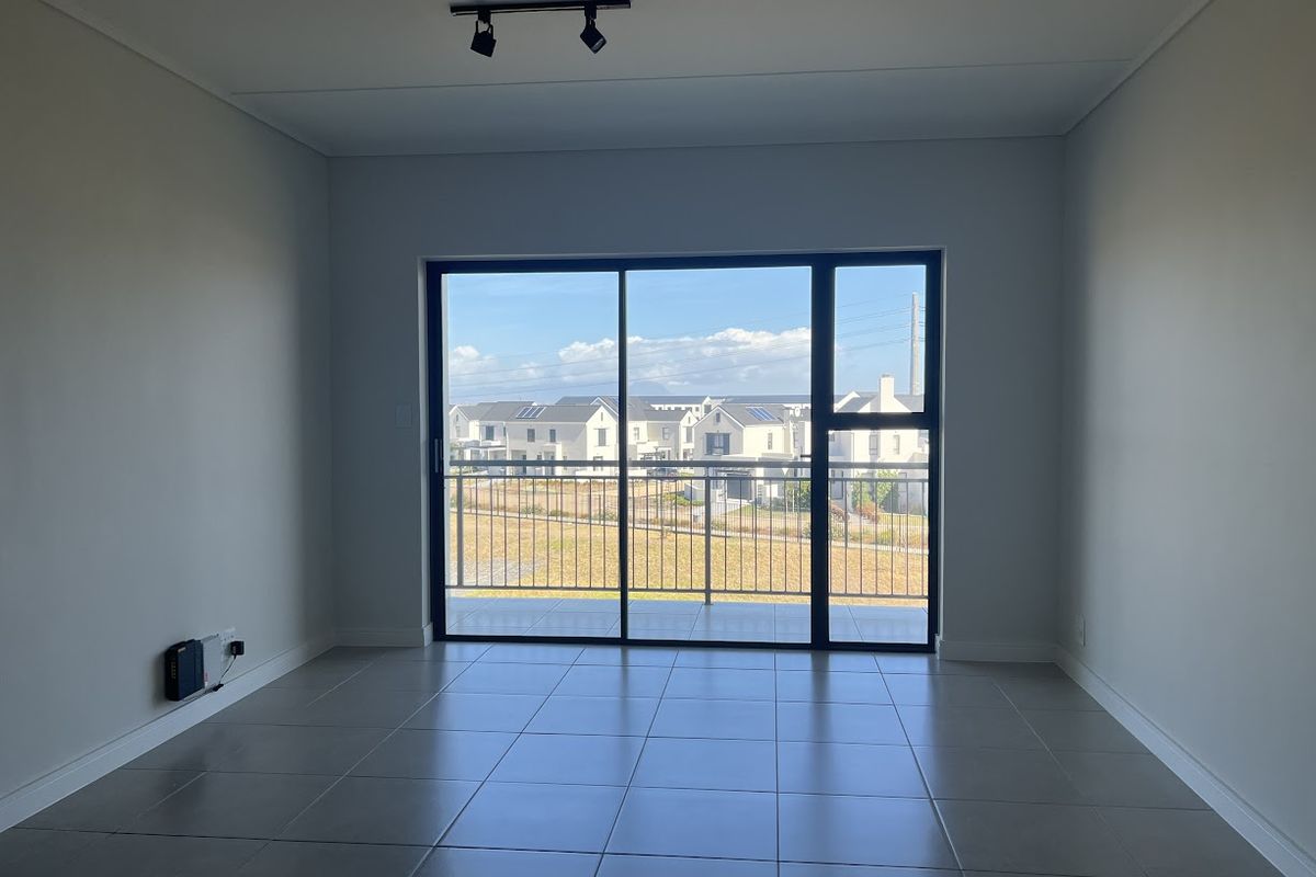 A bright, empty living area featuring large sliding glass doors that open onto a balcony with neighborhood views and modern tiled flooring.