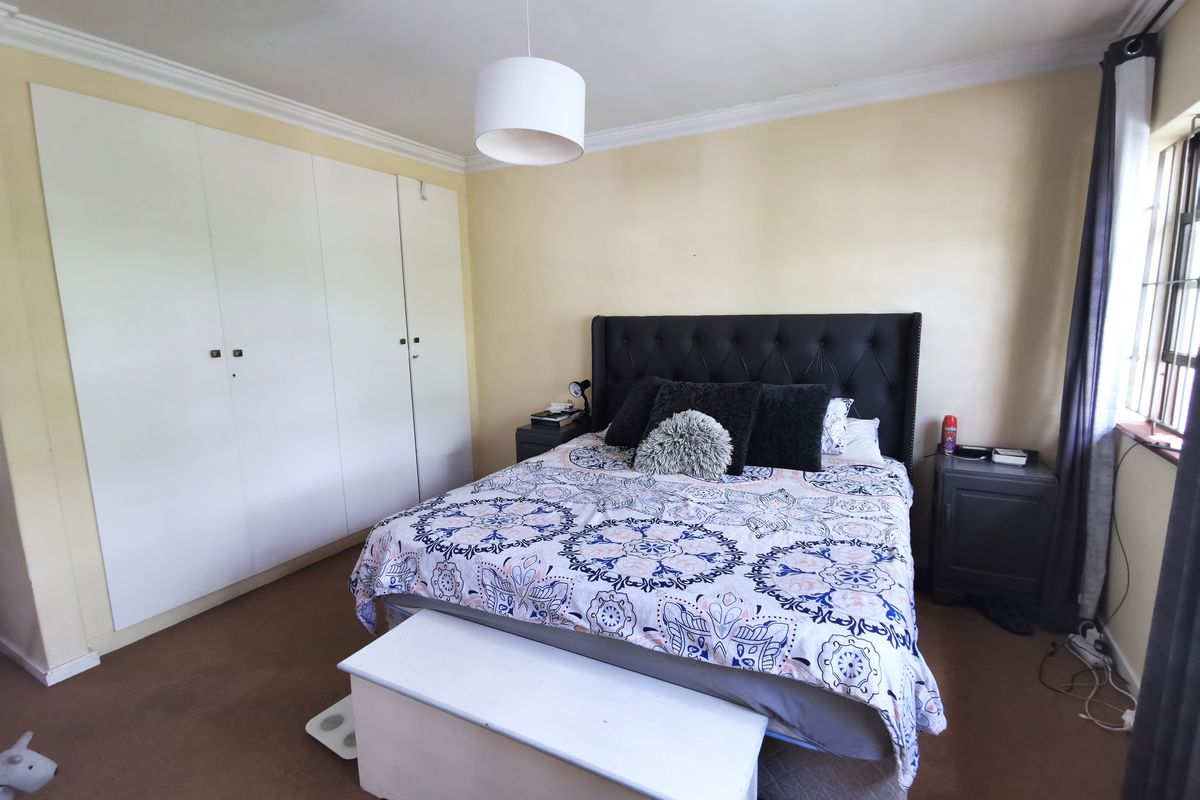 A bedroom featuring built-in white wardrobes, neutral wall finishes, and a window with security bars.