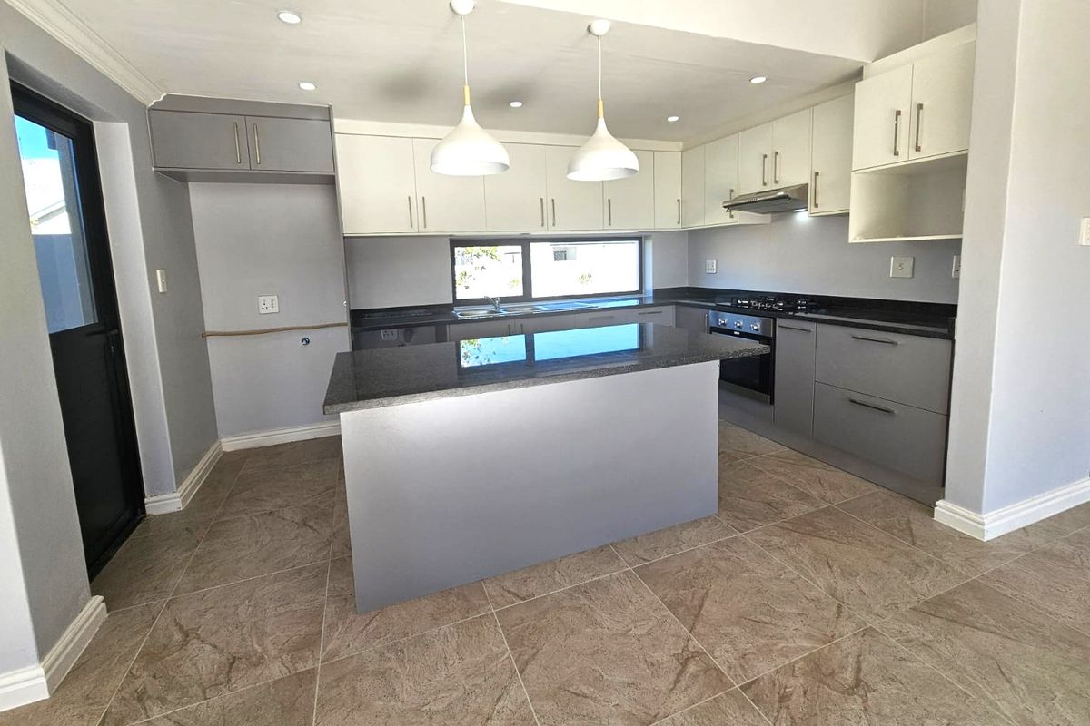 Modern kitchen featuring a central island, granite countertops, built-in oven, gas hob, extractor fan, and ample cabinetry with neutral tiled flooring.